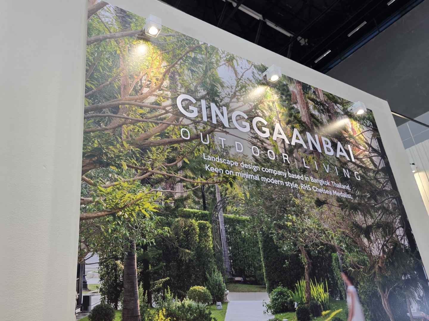 A promotional wall for GINGGAANBAI Outdoor Living, showcasing their lush landscape design with modern minimal style.
