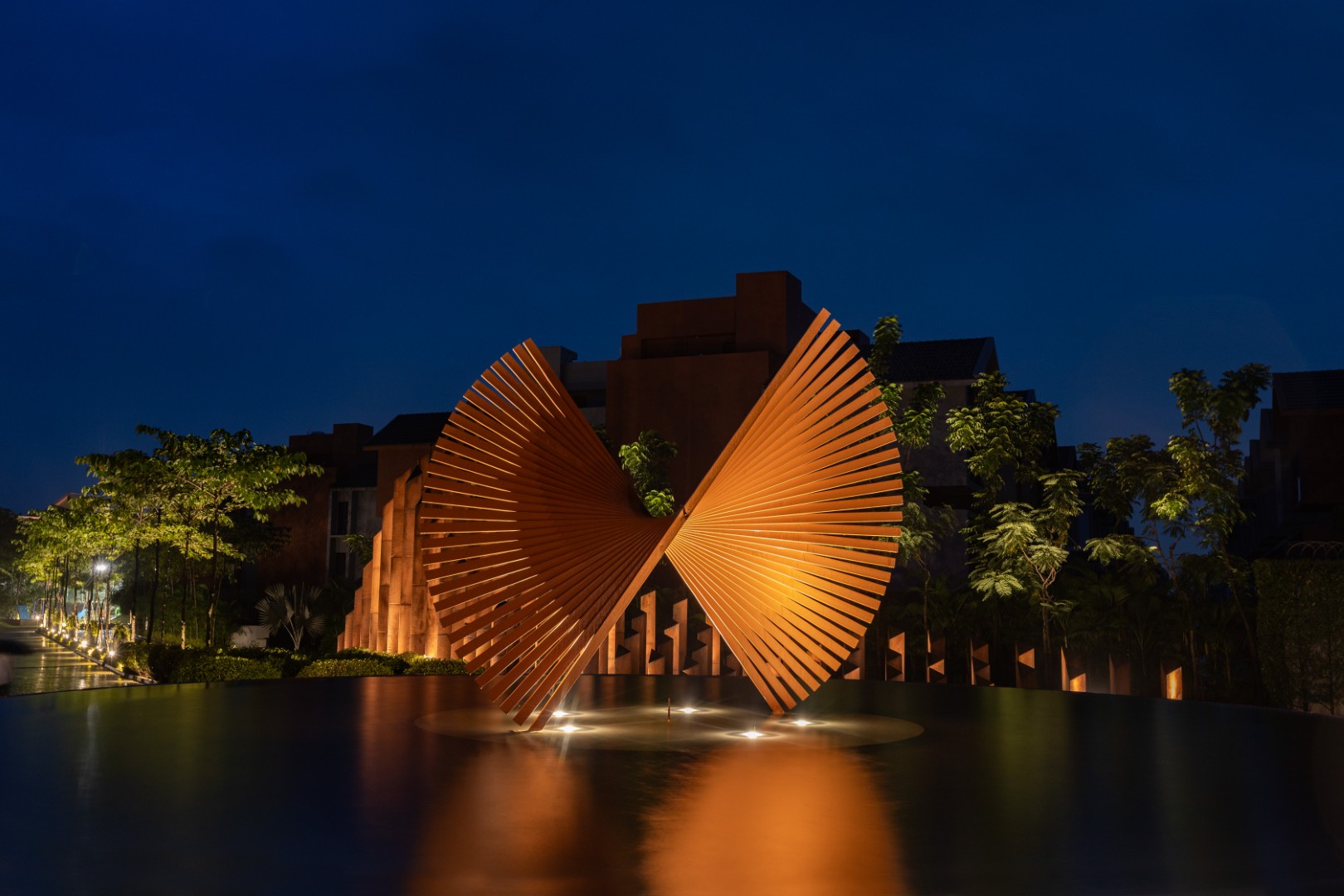 Illuminated golden sculpture over reflective water at modern residential entrance.