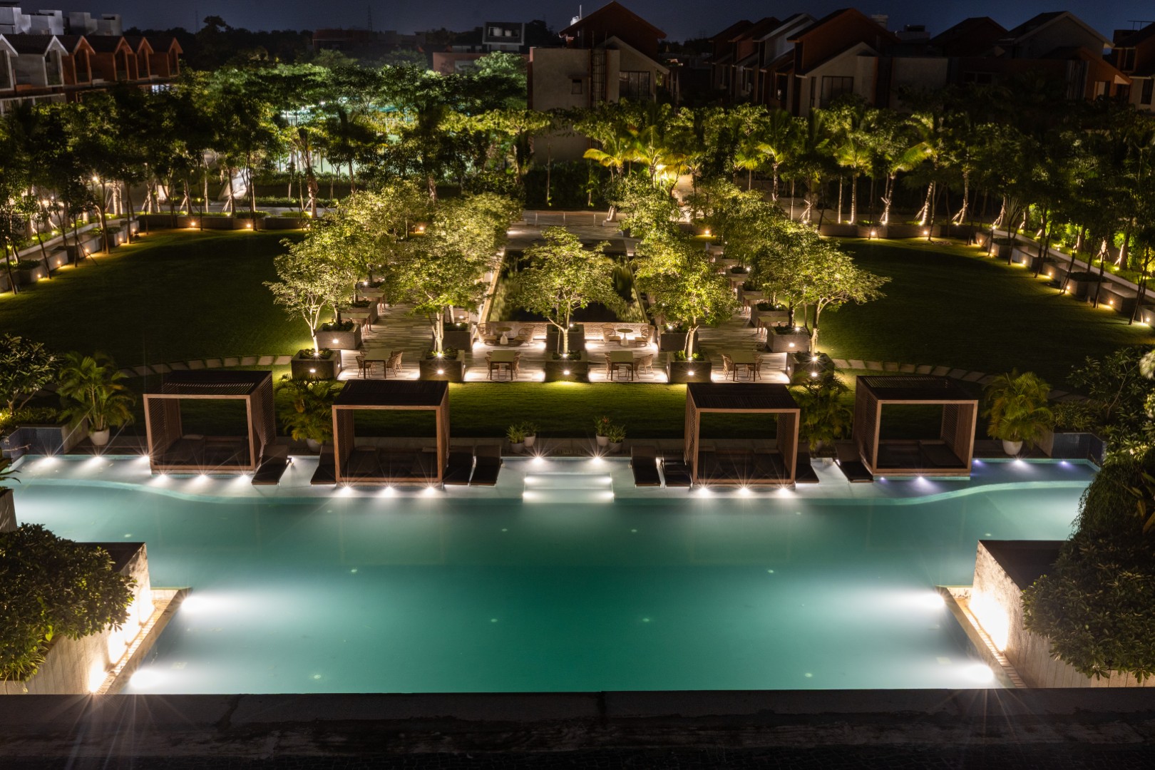 Night view of illuminated swimming pool and landscaped garden in modern residential complex.