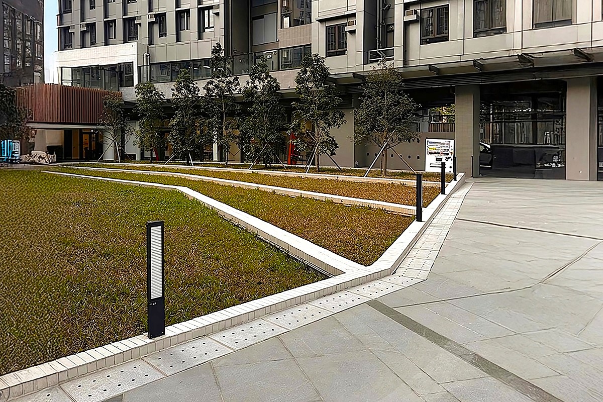 Modern outdoor landscape with ZOID bollard lights lining a tiled walkway near a commercial building.